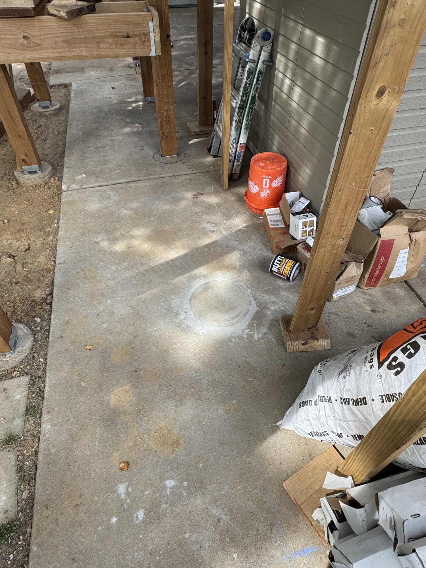 A core-drilled deck footing location filled and finished flush with an existing concrete patio