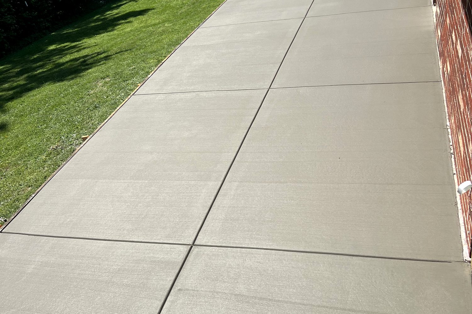 Broom-finish concrete patio along a brick house, poured by Maniaci Construction